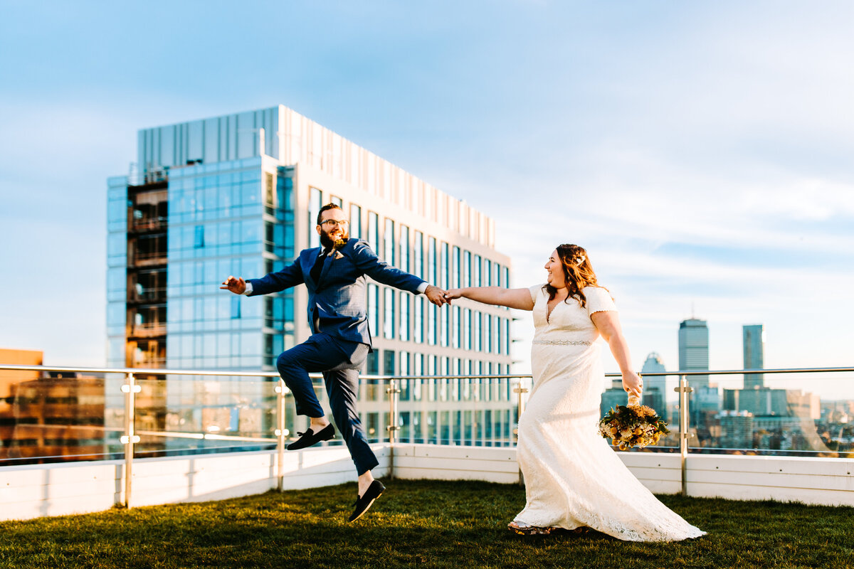 a photo of a bride and groom leaping and dancing on a roof in boston massachusetts on their wedding day