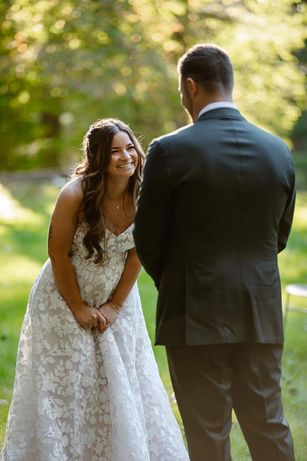 A bride is bent over laughing as her husband reads his vows to her during their summer camp wedding.