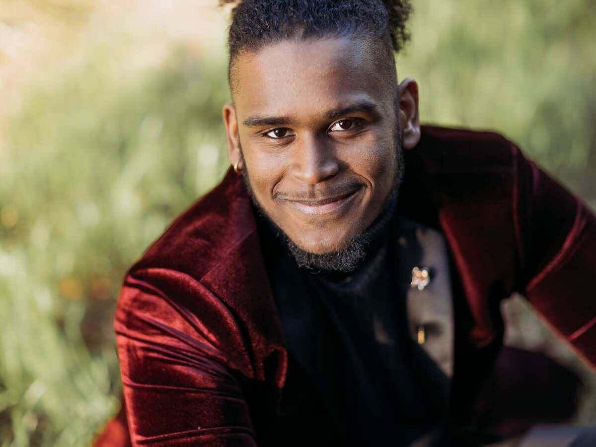 A senior smiling up at the camera for his portrait while wearing a sharp red suit.