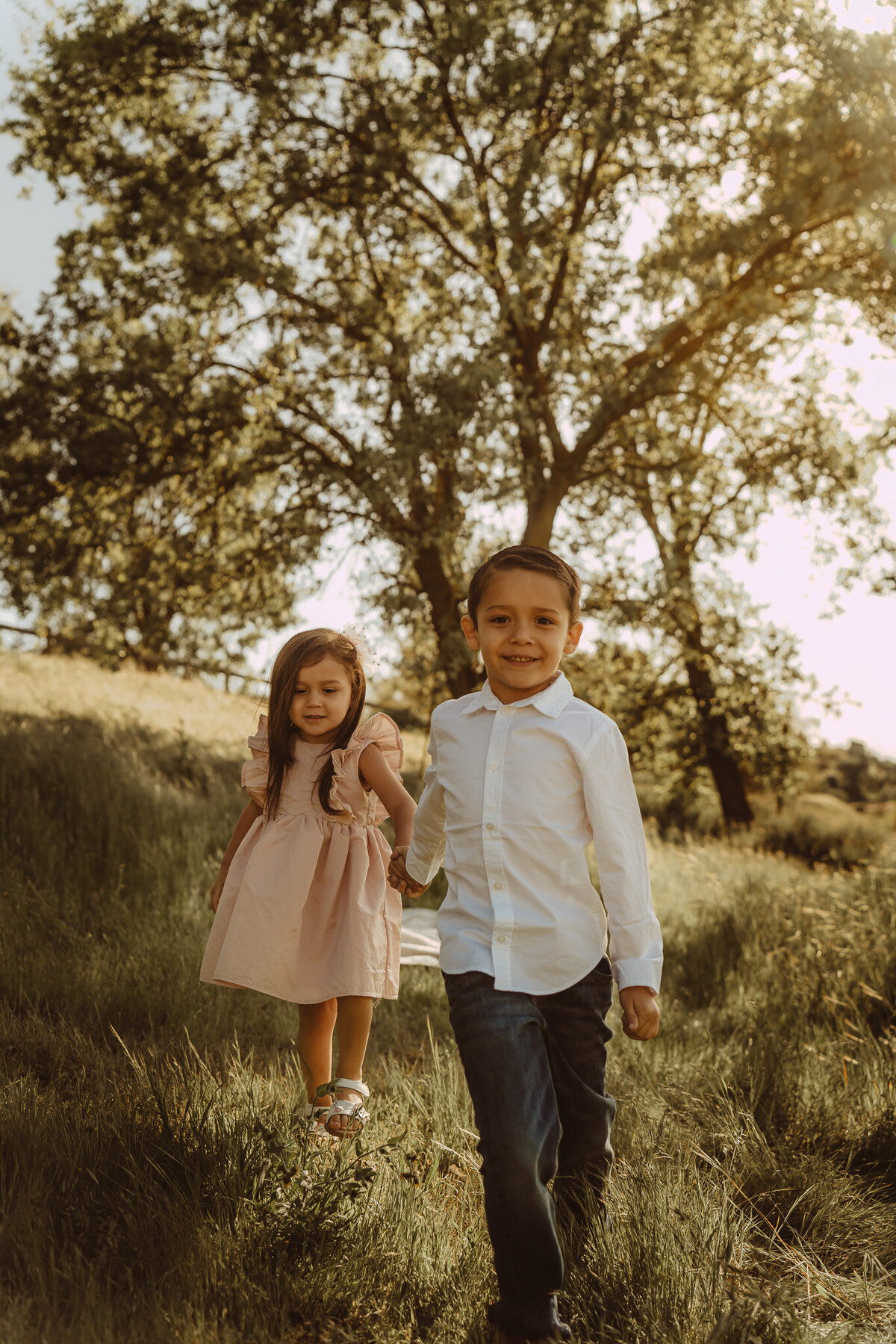a little boy and a little girl holding hands, walking on tall green grass