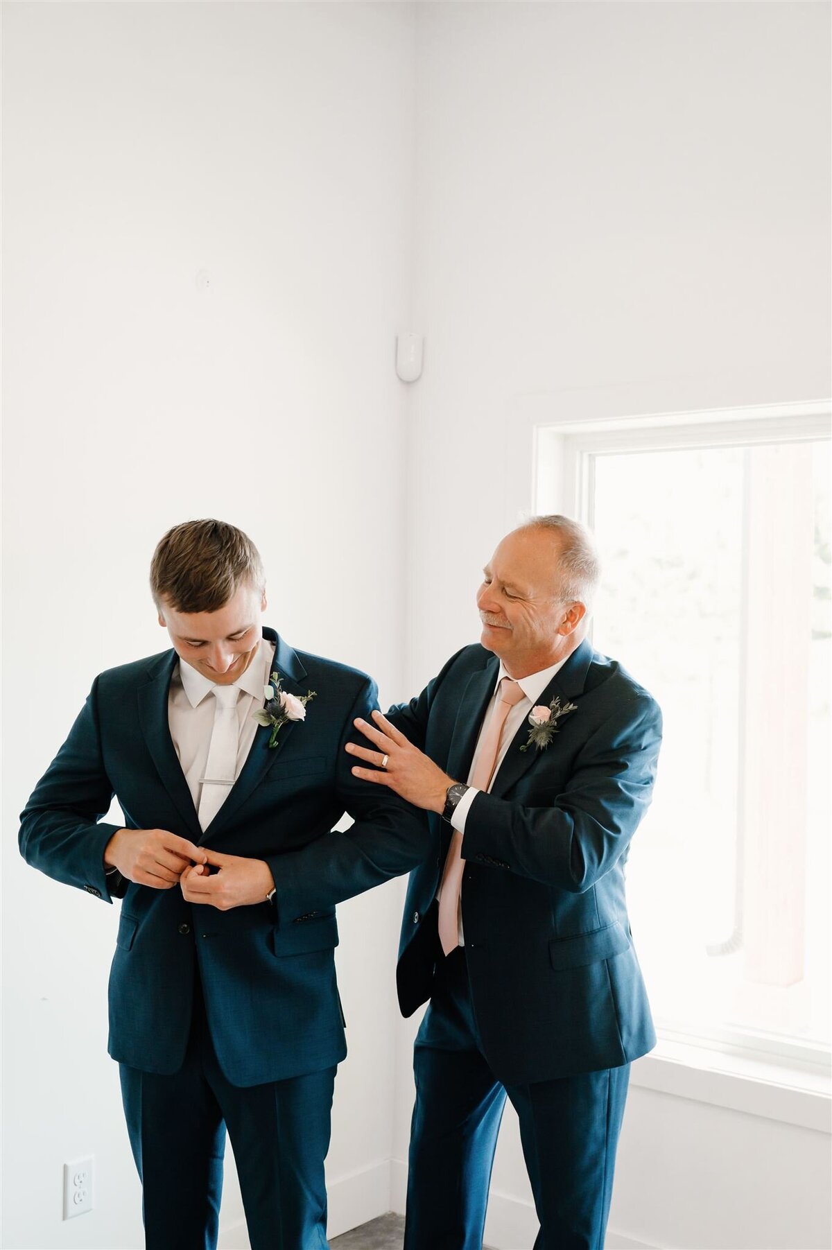 Dad helps groom put on suit jacket at wedding in Bemidji, MN