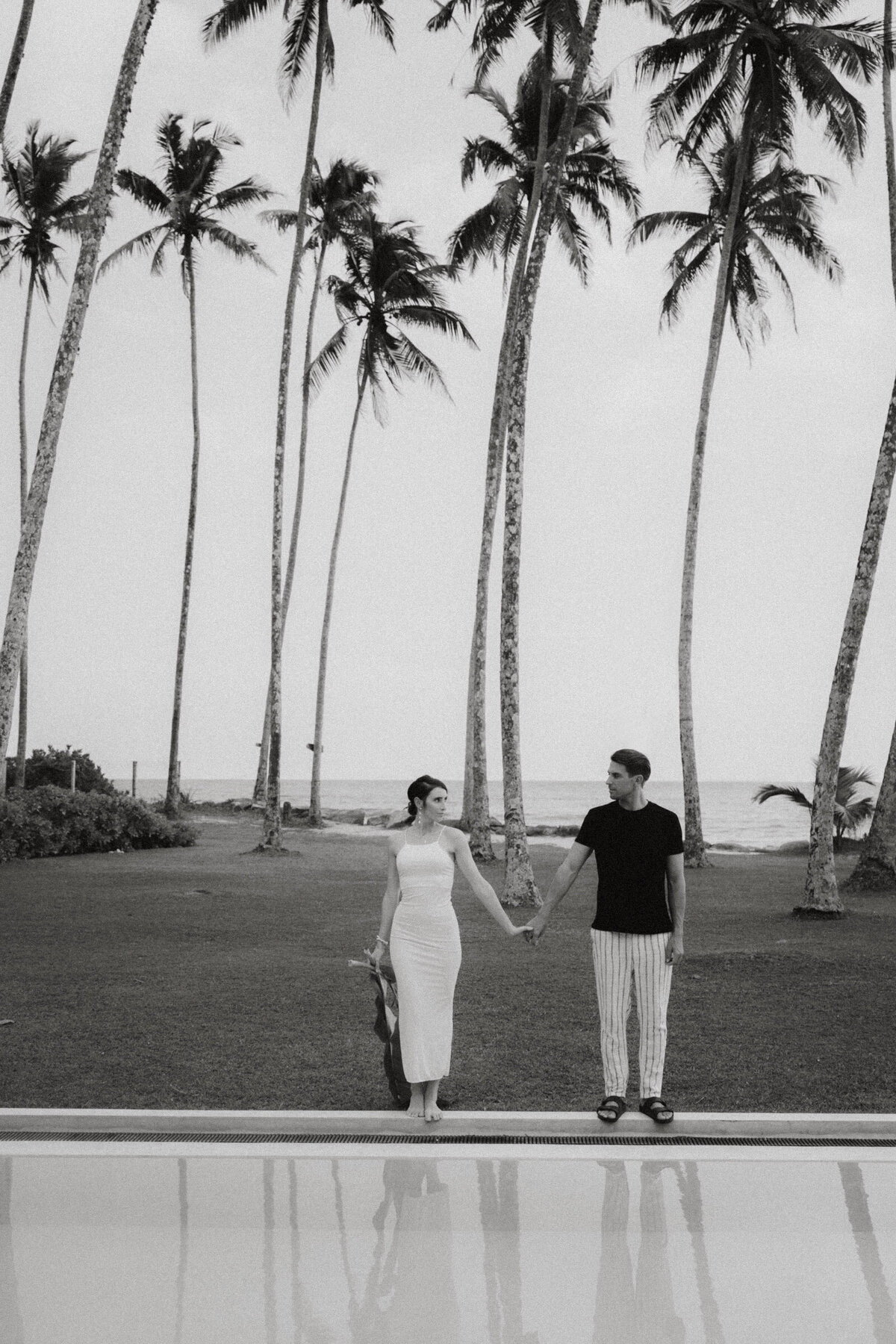 Black and white image of couple walking among palm trees in tropical destination wedding