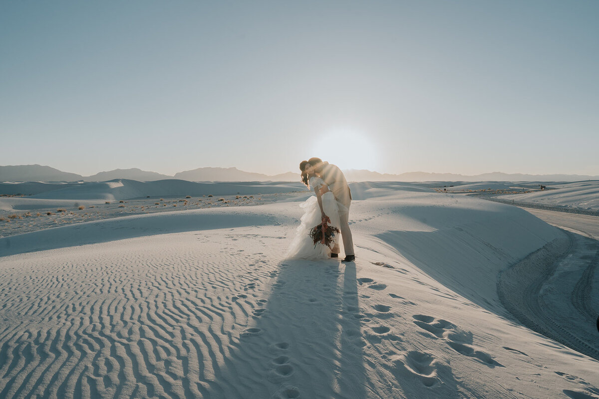 Couple standing on white sands with the sun shinning through.