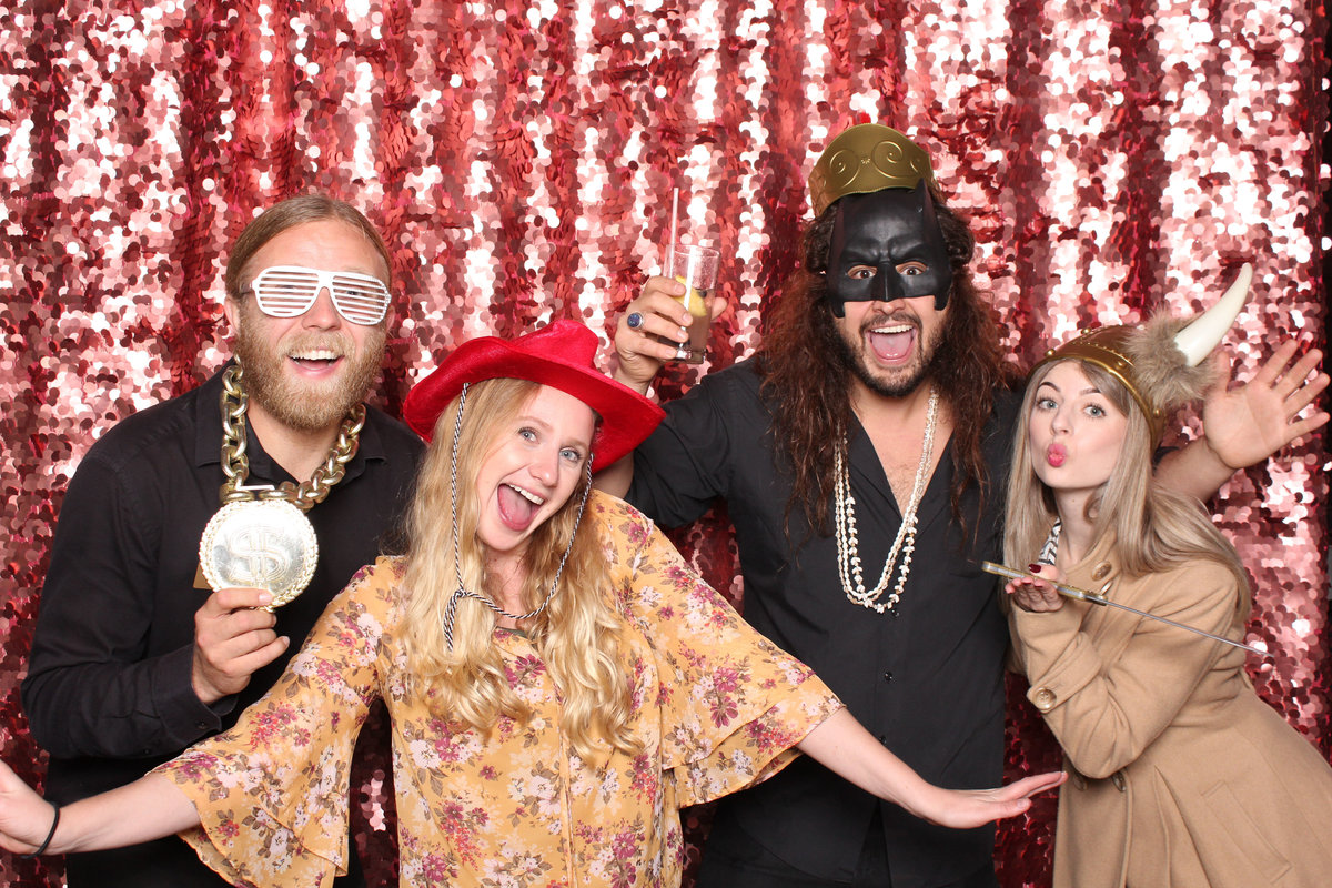 Two couples wearing props have fun together in a photo booth