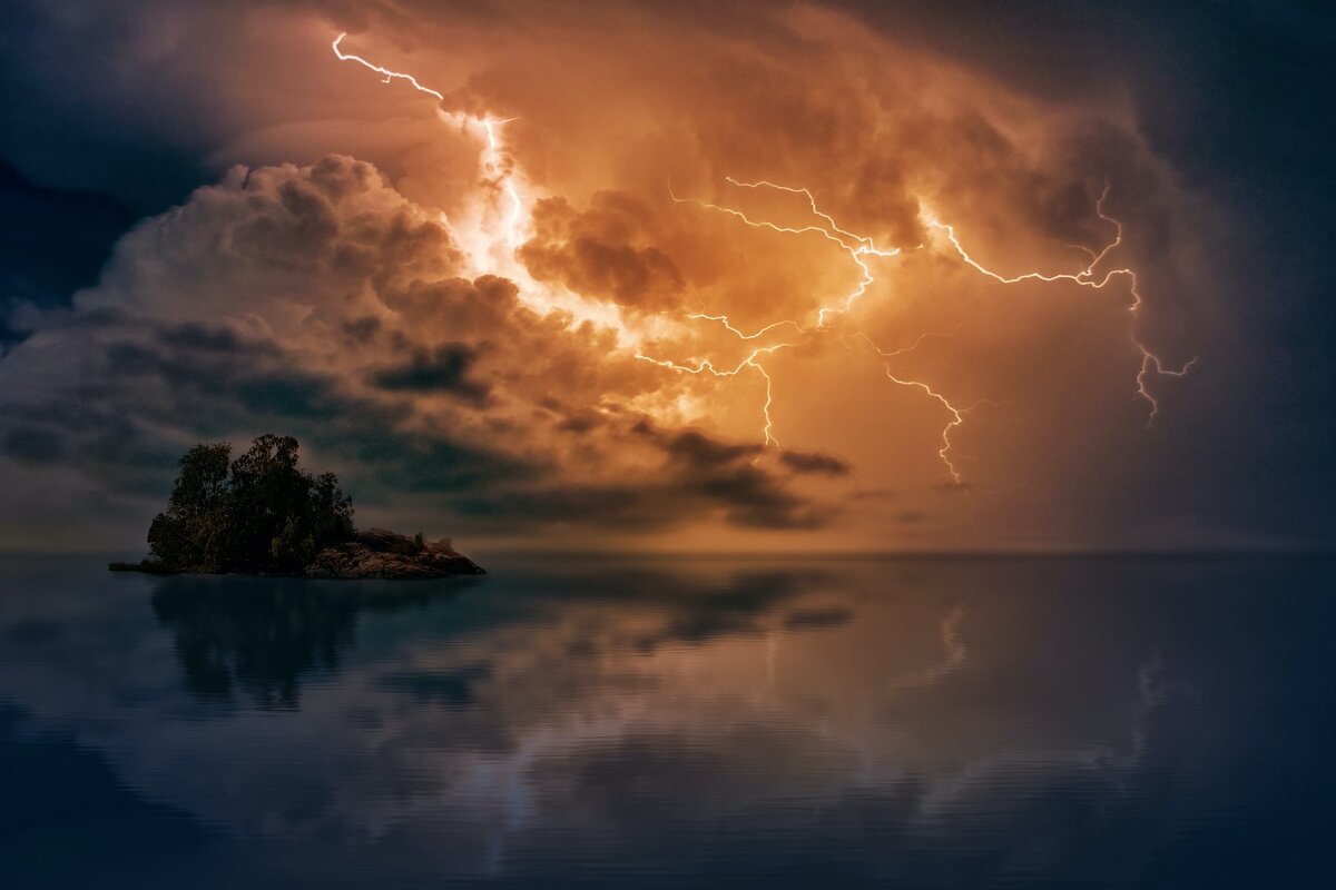 lightning bolts shooting across the sky above water an a small island