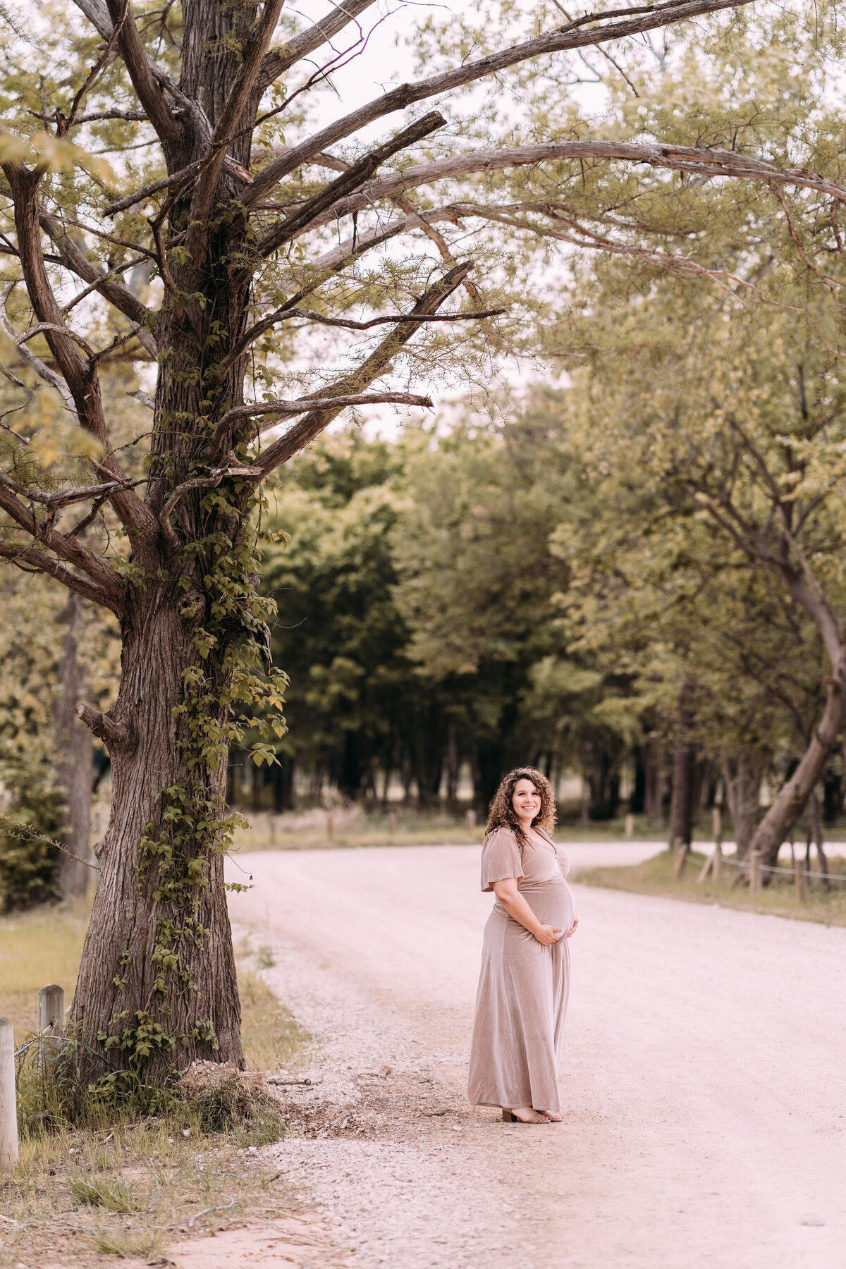pregnant woman stands beneath tree