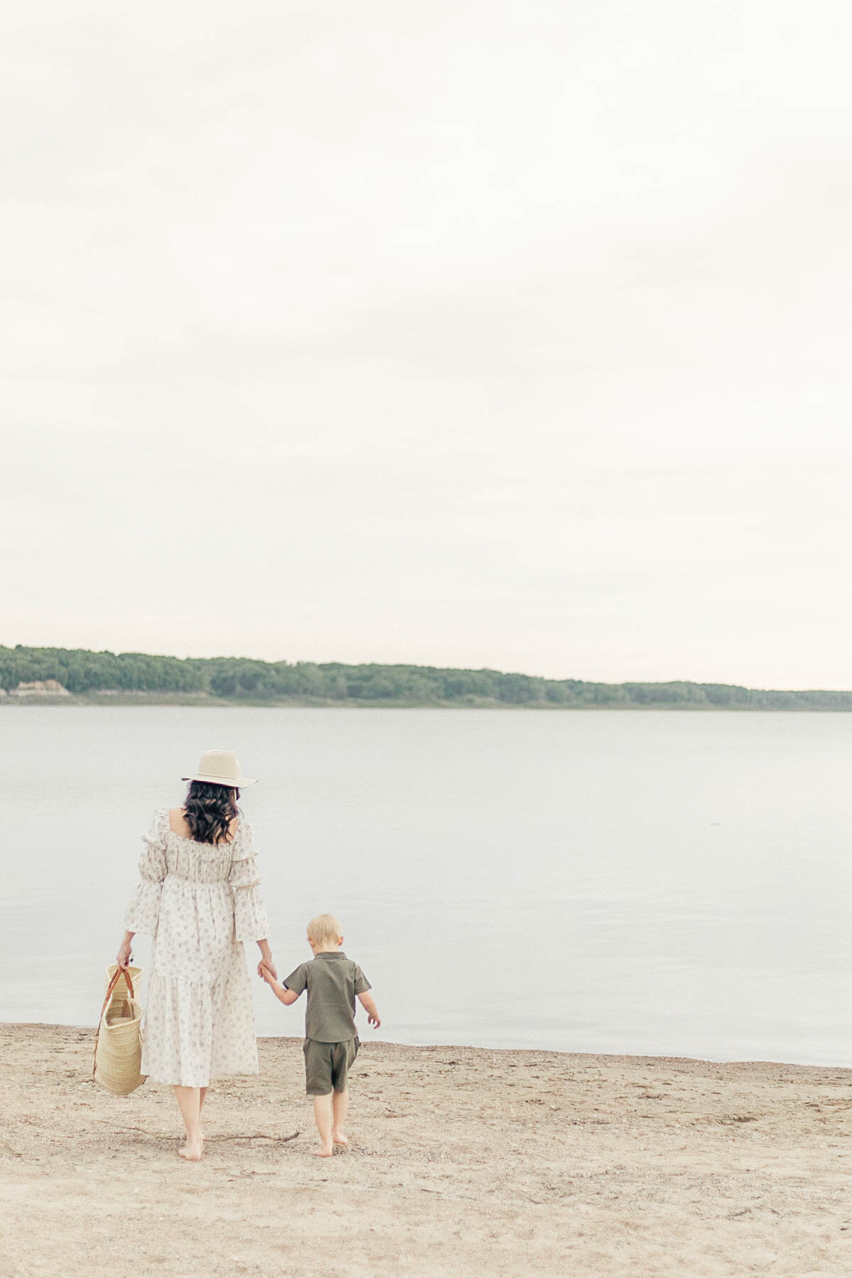 Mom and toddler son walking hand-in-hand toward the water during a Kansas City beach session with their family of six.