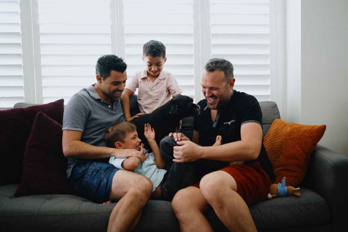 Two dads tickle their twin sons on the couch during their family photoshoot.