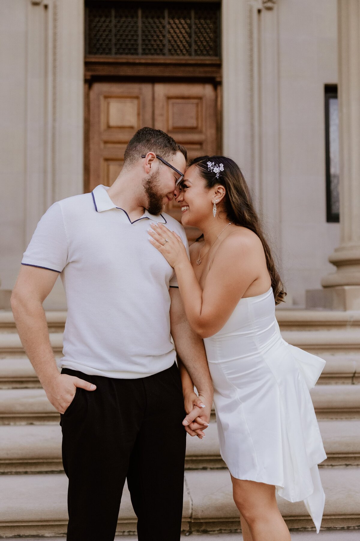 Engaged couple holding hands and touching foreheads while smiling in front of a building's steps, captured by a Hudson Valley engagement photographer.