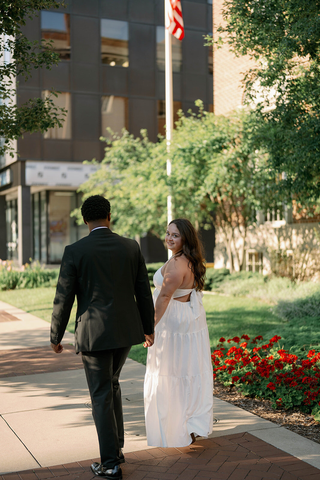 Kalamazoo engagement session with couple walking hand in hand near garden flowers.