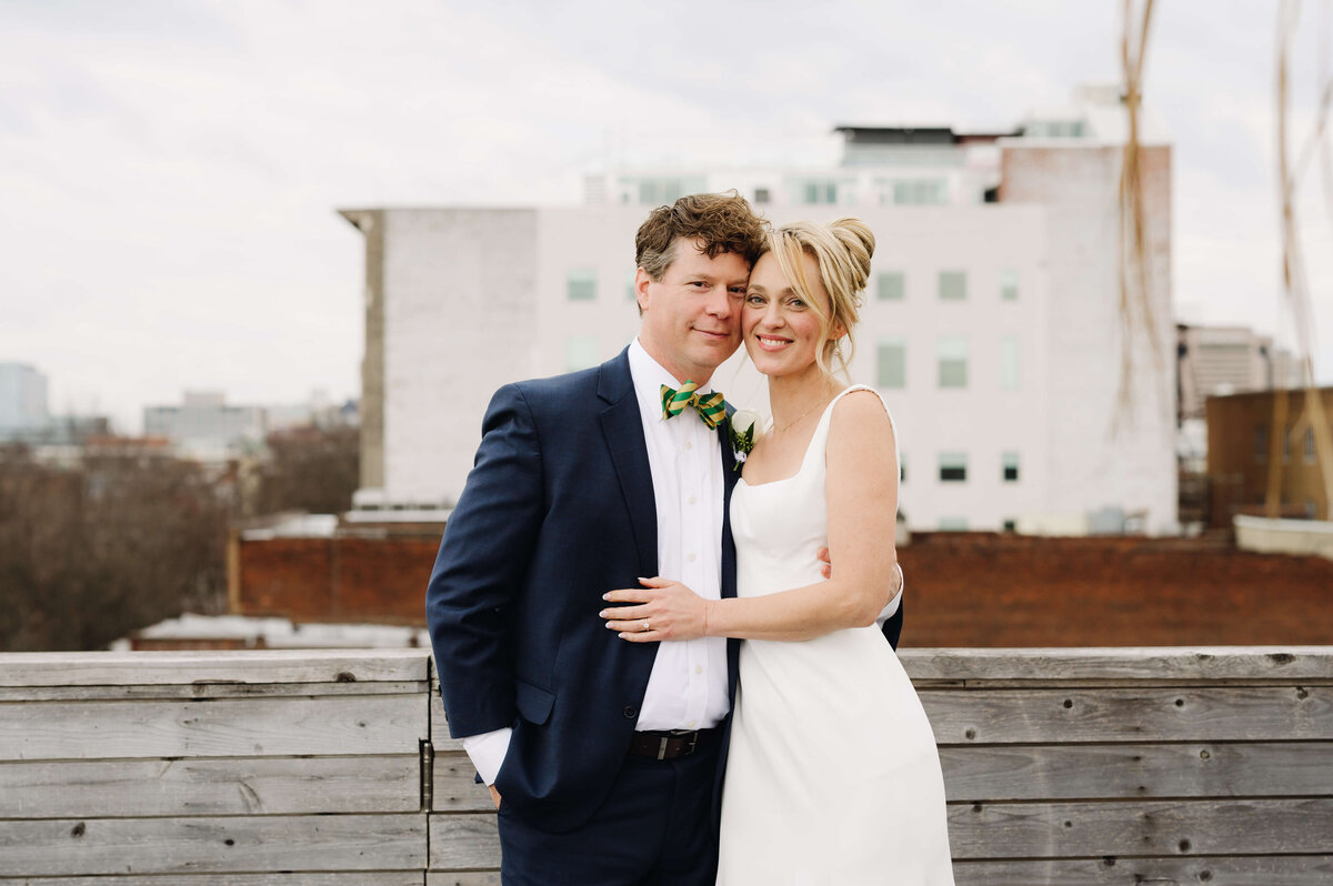 common house richmond wedding roof top photo with groom in a blue suit coat holding his blonde bride as they lean into one another