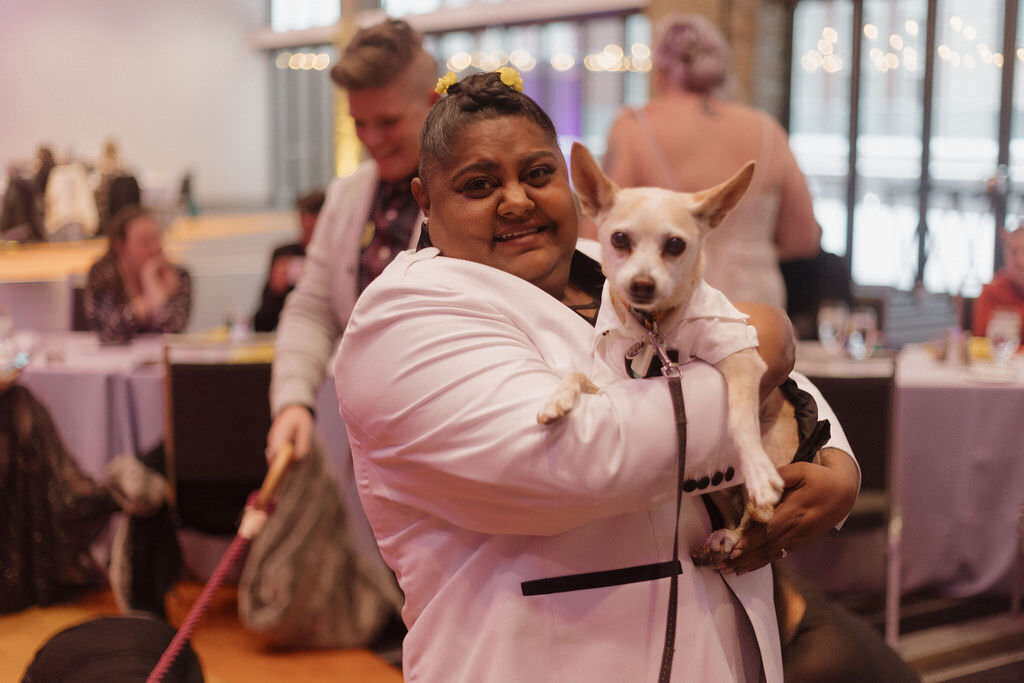 A newlywed holding a small dog in their arms.