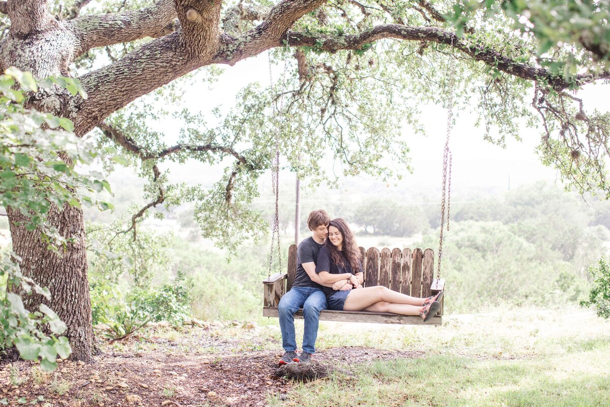 Texas couple embrace on swing under oak tree in wedding engagement session by Firefly Photography