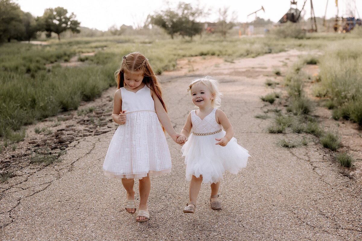 Two little girls walking on a pathway holding hands.