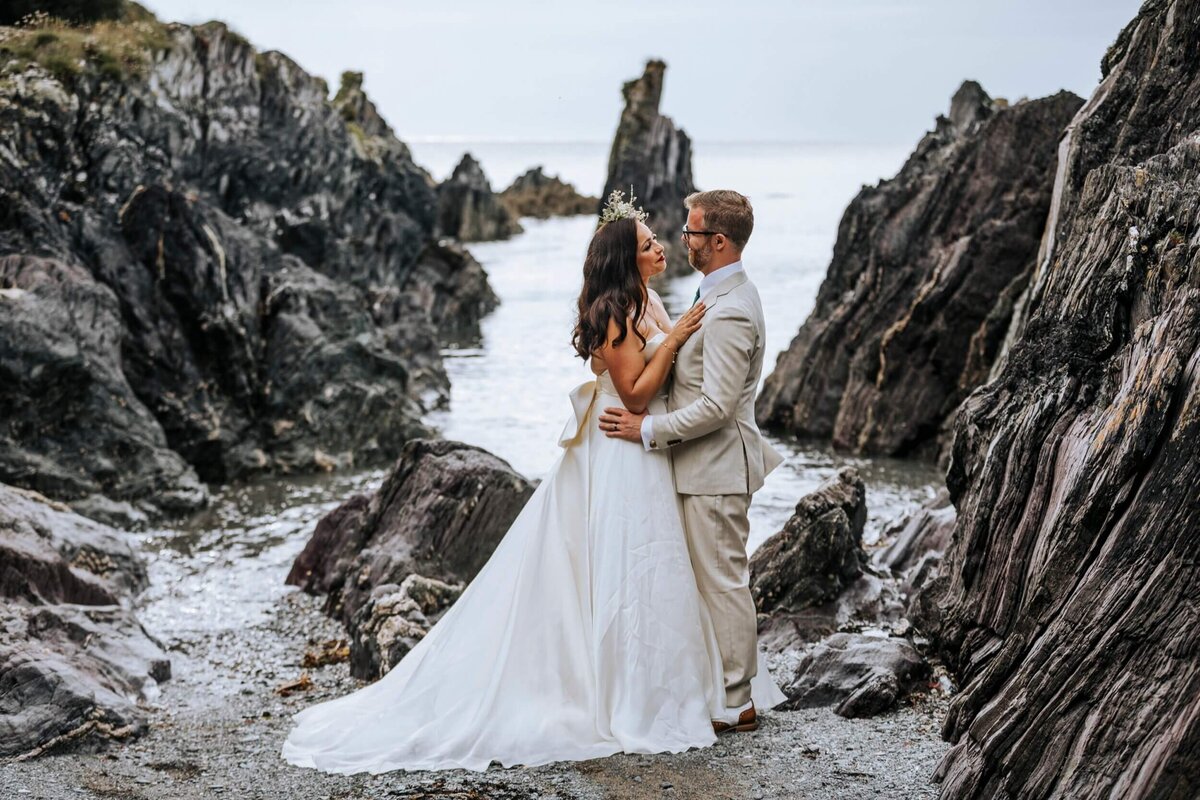 A bride and groom standing on a rocky beach