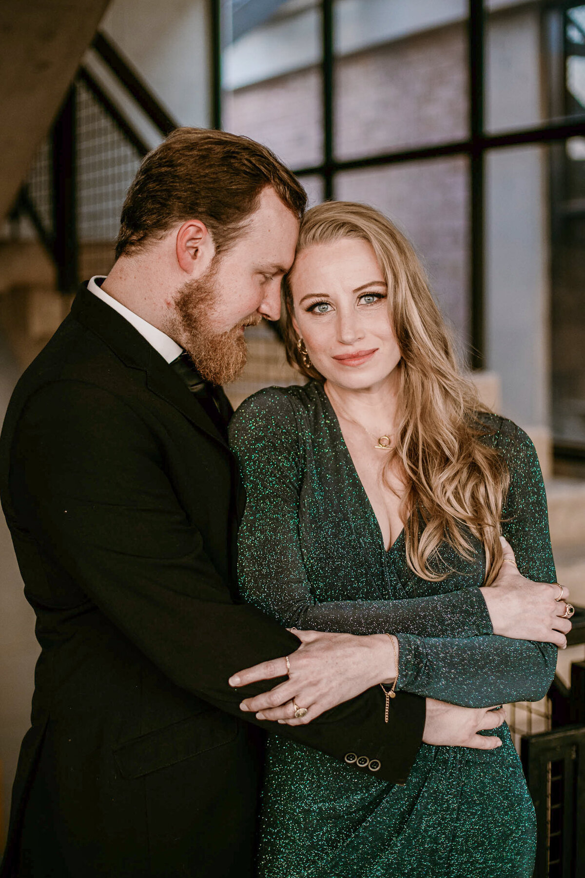 A couple where the one partner is caressing his fiancée, wrapping his arms around her, and placing his forehead onto her cheek. 