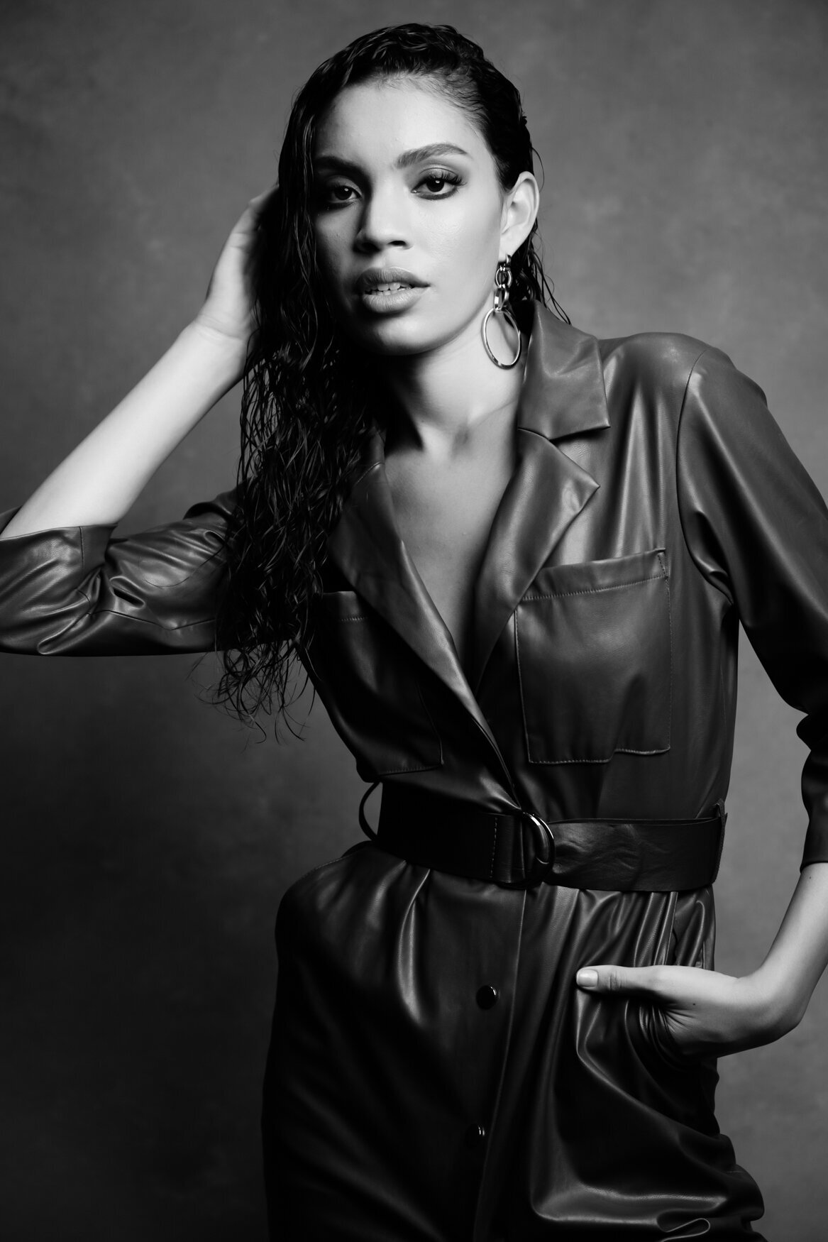 woman with long hair posing to the camera touching her hair with her right arm and the left arm on her pocket