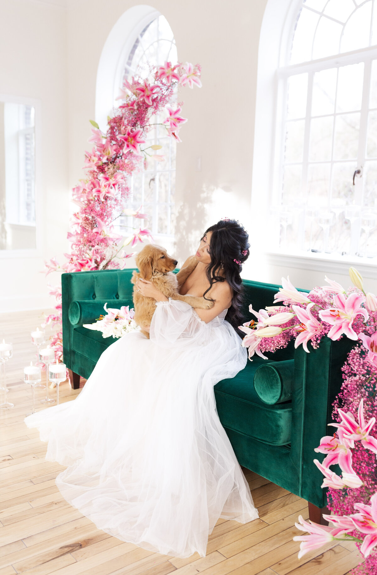 bride sitting on emerald green sofa with puppy surrounded by pink florals