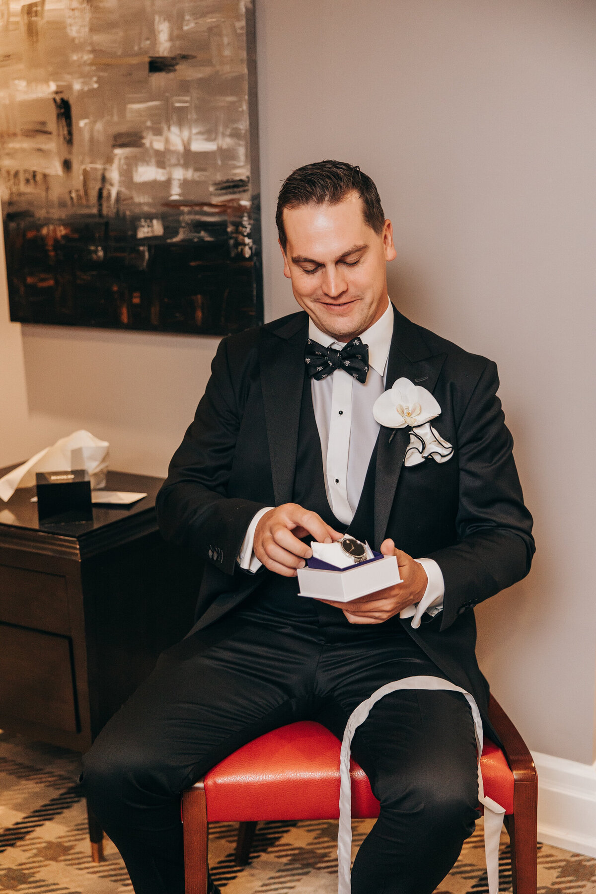 A groom in a black tux opening a gift from his bride