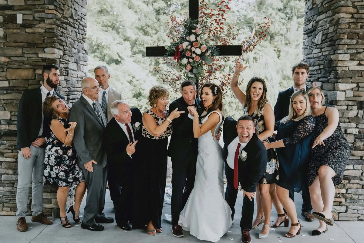 A playful wedding photo of the bride and groom with their bridal party making funny faces and gestures around them.