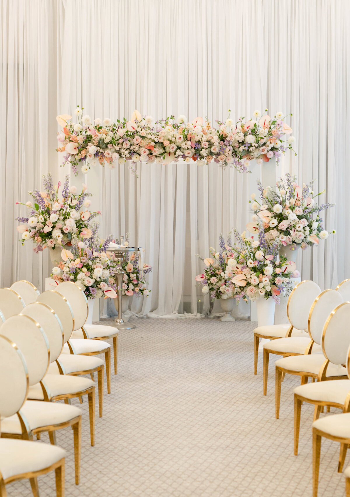 A Four Seasons wedding ceremony with an arch and large arrangements of pastel flowers.  