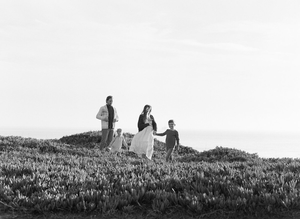 Black and white photo of family with two children on coastal hillside | Rooted Within Santa Barbara family evaluations and guidance