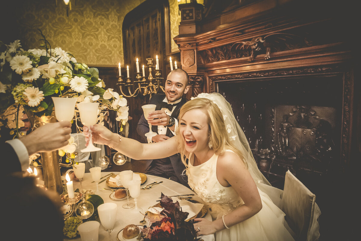 Bride and groom laughing and toasting during their wedding dinner at Château Challain, captured in joyful, romantic fine-art wedding photography.