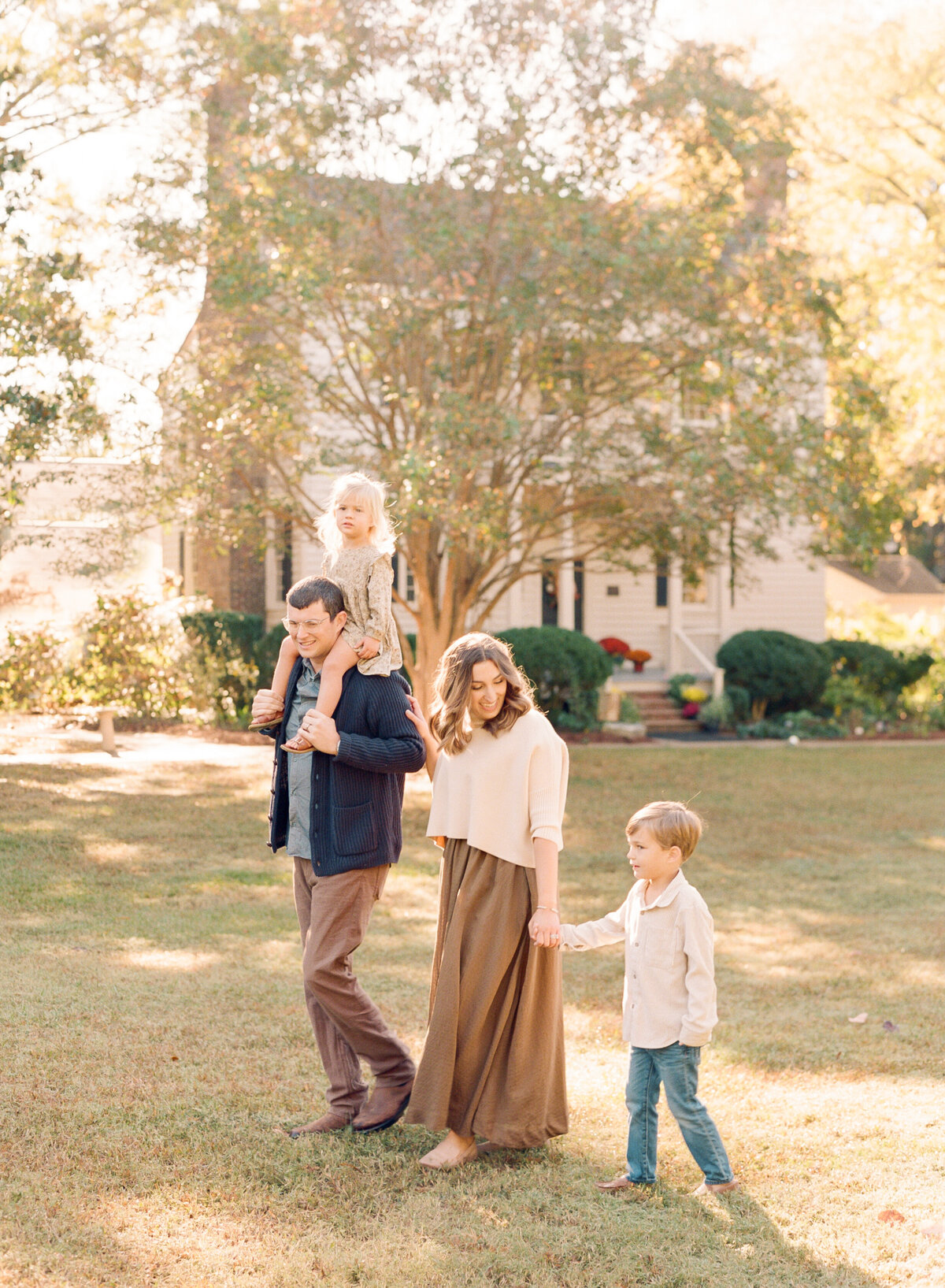 Family smiles and walks through a park in Wake Forest for family photos. Family walking during their family portrait session in Wake Forest, NC. Photographed by Raleigh family photographer A.J. Dunlap Photography.