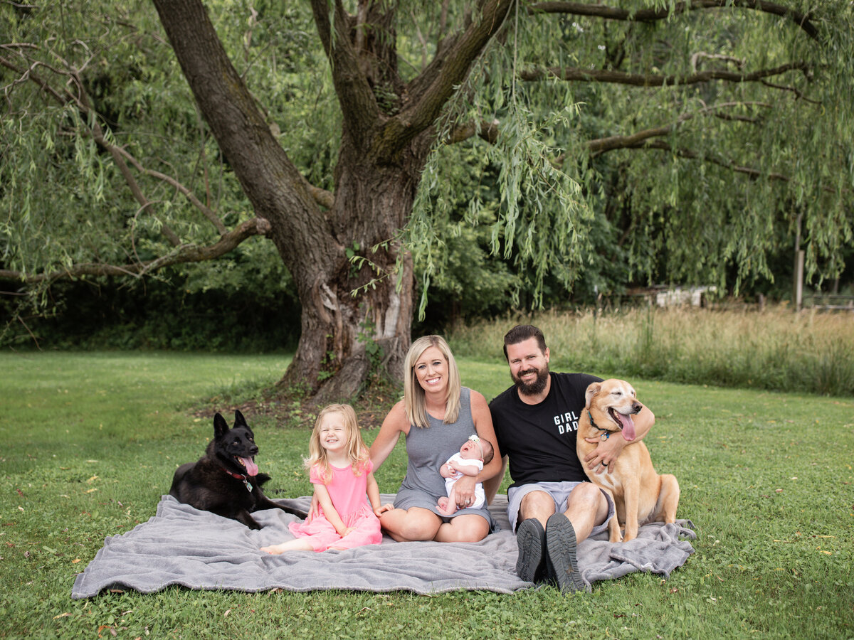 family with two dogs sitting in backyard for in home newborn photoshoot