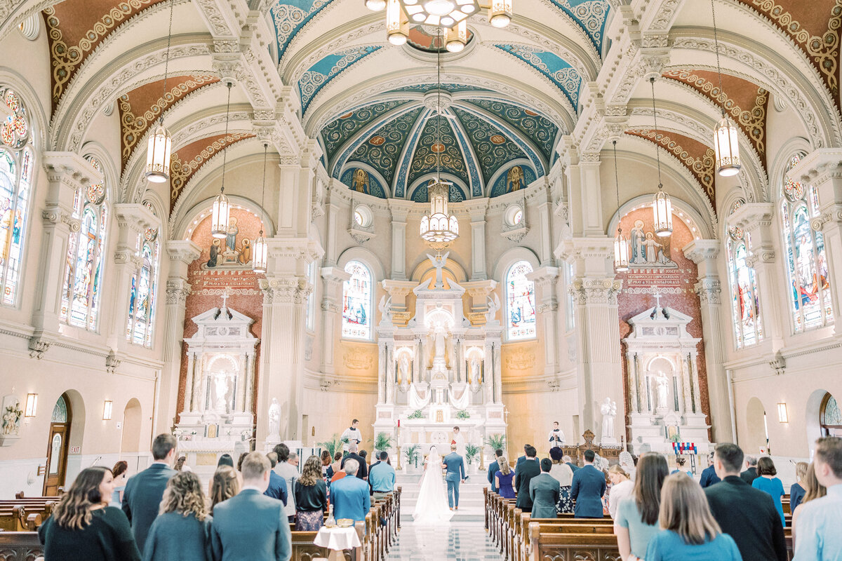 Couple standing at altar and wedding guests standing in pews during St Bernard Catholic Church wedding in Akron, Ohio