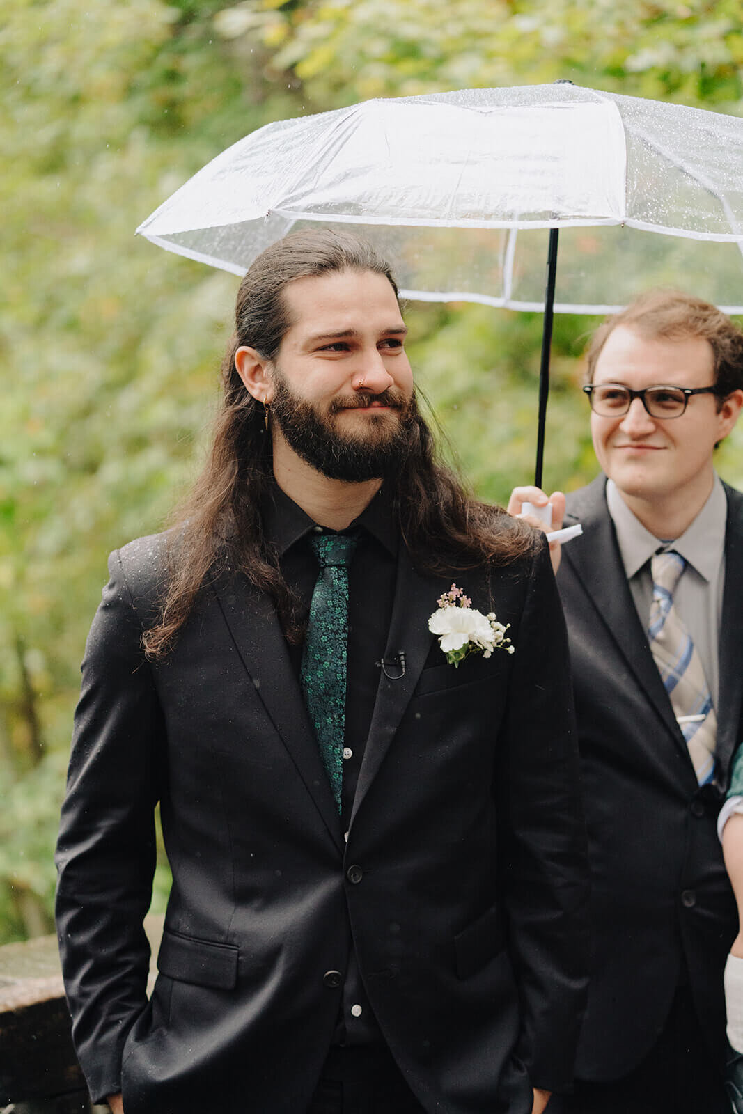 Groom wearing black suit with umbrella held above him