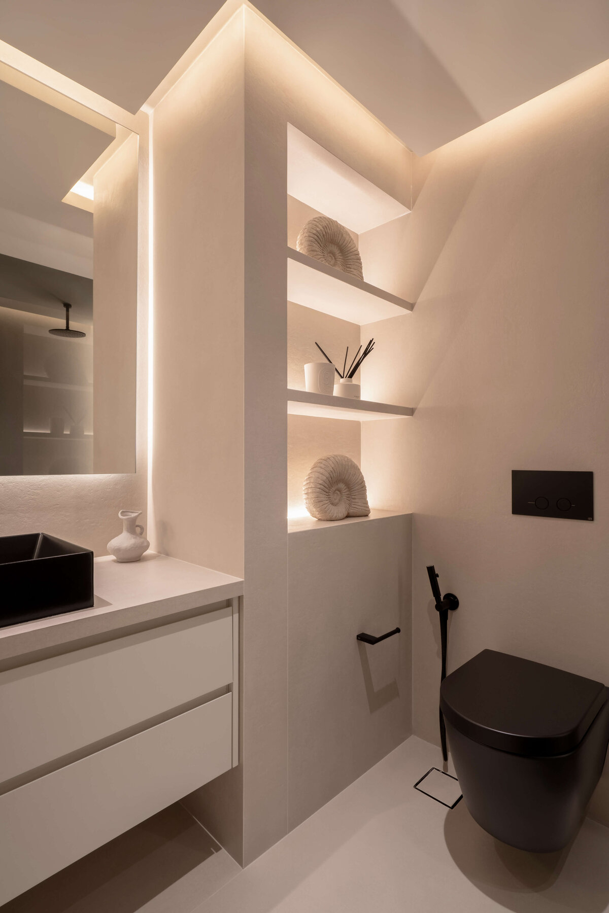 Spacious bathroom with a focus on light, neutral tones. Large built-in shelving emits a soft light. A black sink and toilet add contemporary flair to the space.