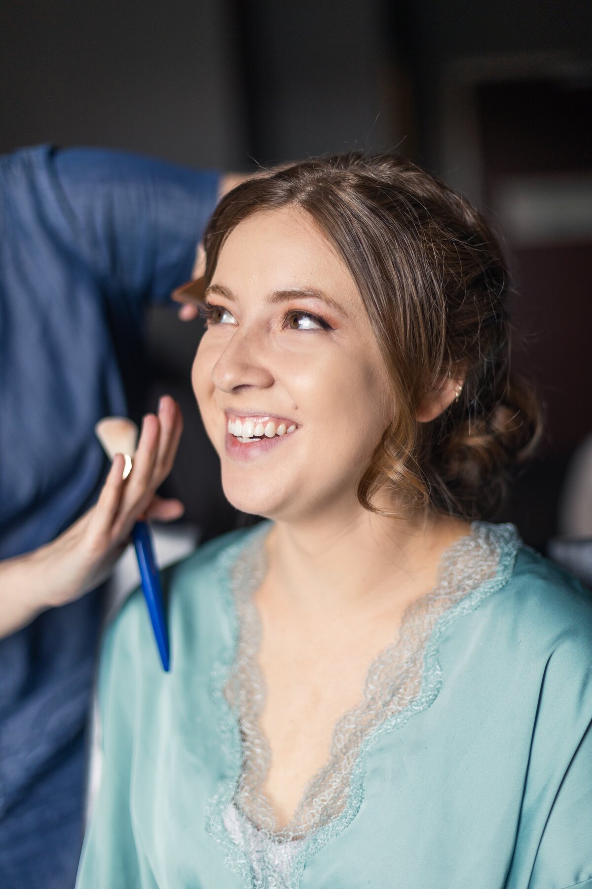 A girl in a blue robe with lace smiles as her makeup is being applied