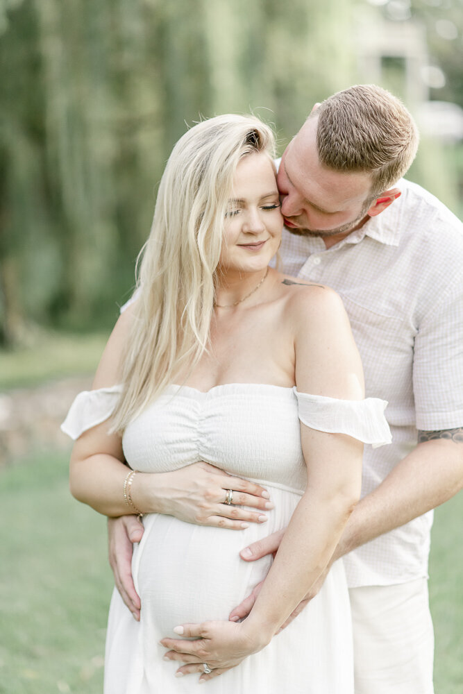 Husband kisses his pregnant wife's cheek in an outdoor Nashville park By Nashville maternity photographer Kristie Lloyd