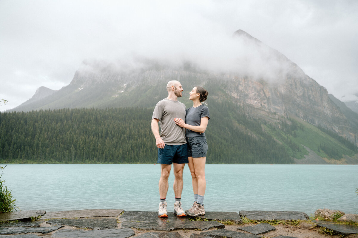 Newly engaged couple looking at each other in front of Lake Louise with Fairview mountain in the background. 