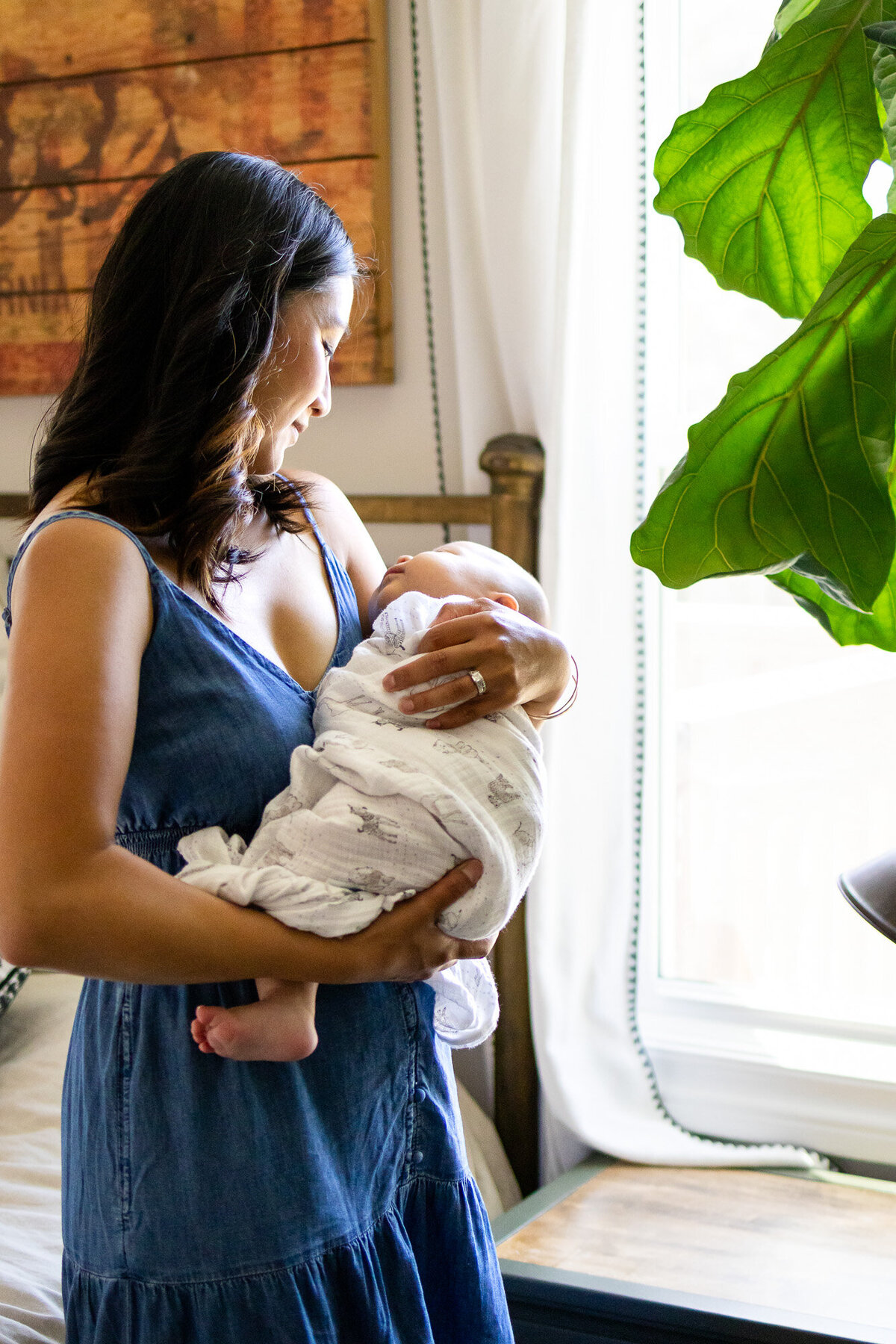 Peaceful scene of mother swaddling newborn by window light, documented by San Francisco newborn photographer.