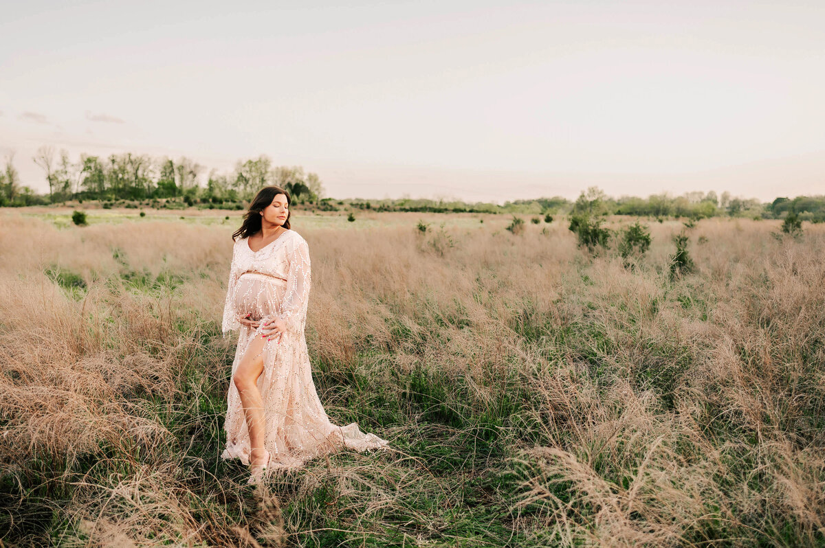 pregnant mom in floral dress hugging belly at a field captured by Joplin MO maternity photographer Jessica Kennedy of The XO Photography