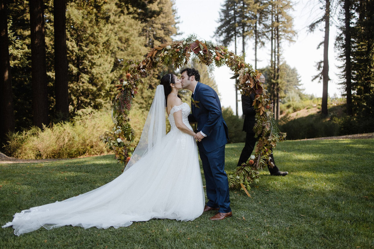 Romantic circular floral arch for outdoor wedding ceremony with bride and groom kissing