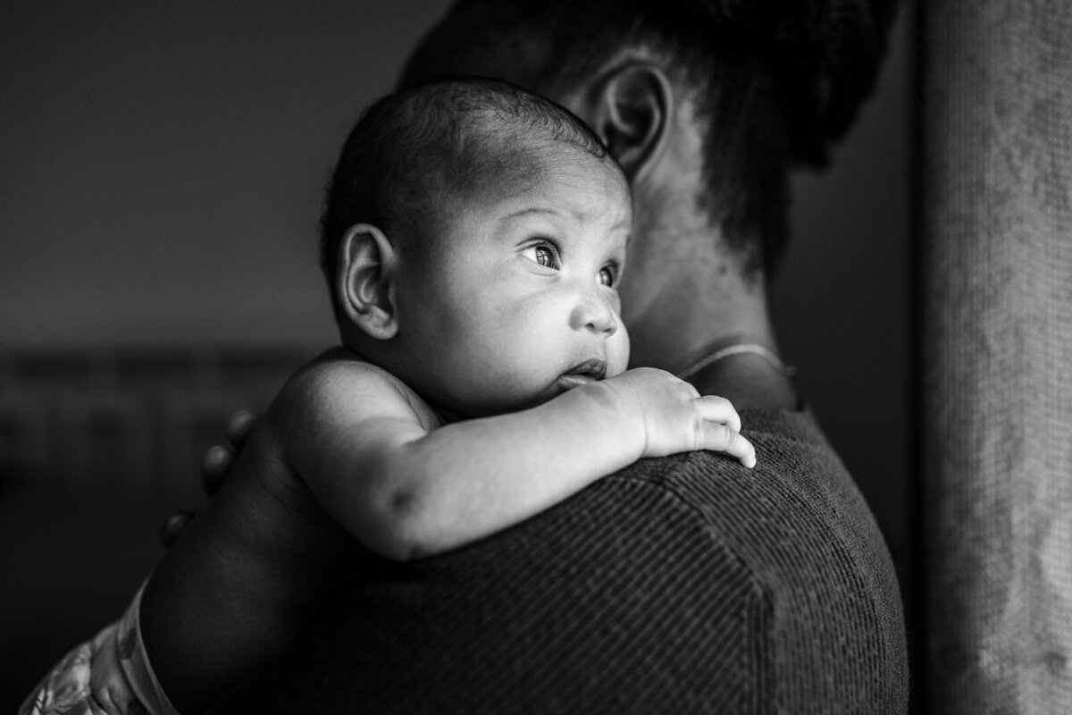 newborn resting on mom's shoulder with eyes open looking towards light