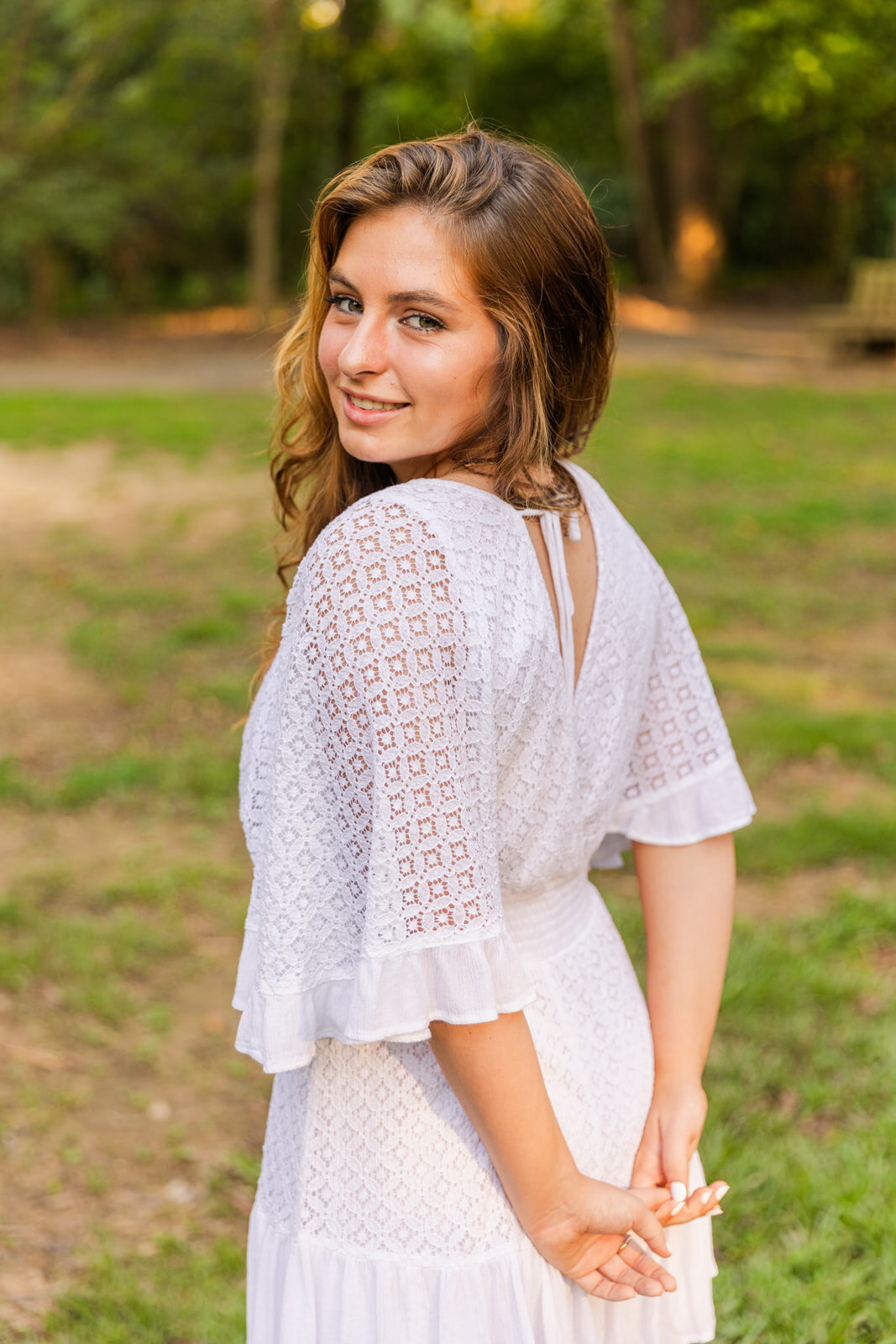 young woman wearing a white dress looking over her shoulder her hands together in the back