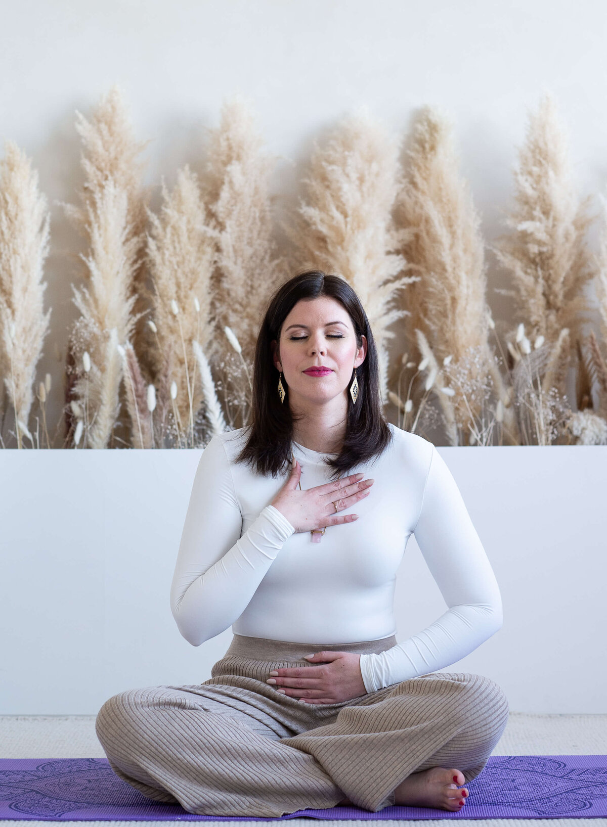 Ottawa branding photography of a woman in a white yoga outfit sitting on the ground doing breathwork exercises.  Captured at Skye Studio by JEMMAN Photography
