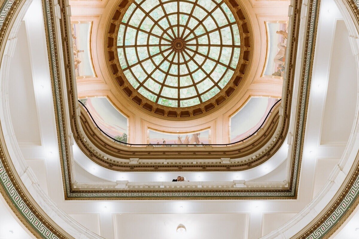 Glass dome at Douglas County Courthouse with newlyweds kissing after their courthouse wedding in Omaha.