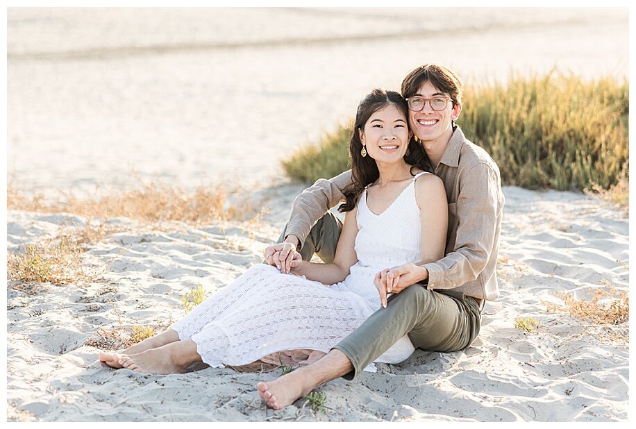 engaged couple sitting in Coronado sand dunes