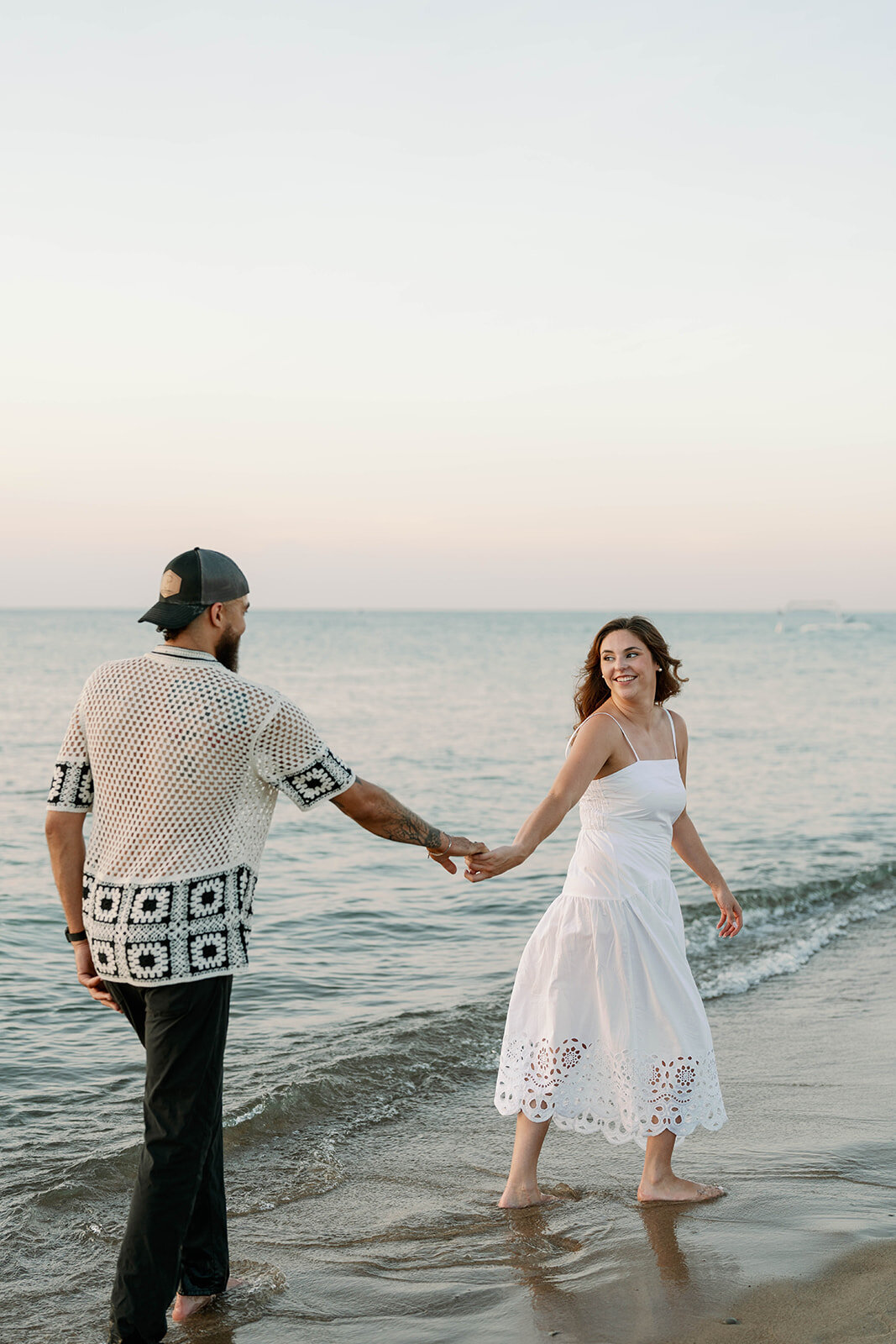 Engaged couple holding hands and walking through the water during their Lake Michigan sunset photos