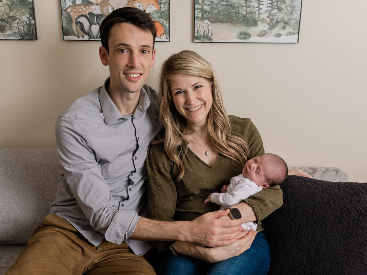mom and dad sitting on couch holding newborn baby boy for in home lifestyle session