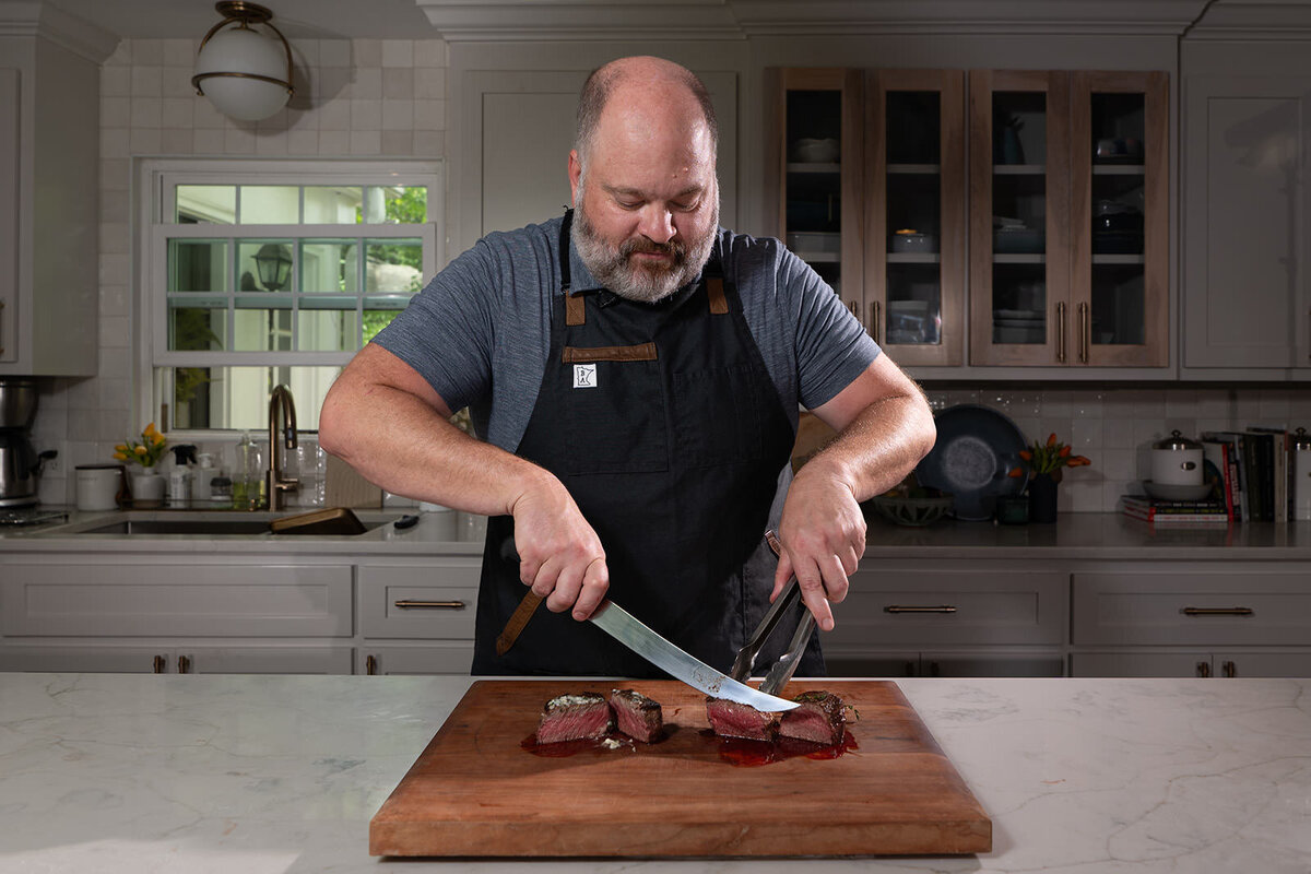 A person cutting steak on a wooden cutting board 