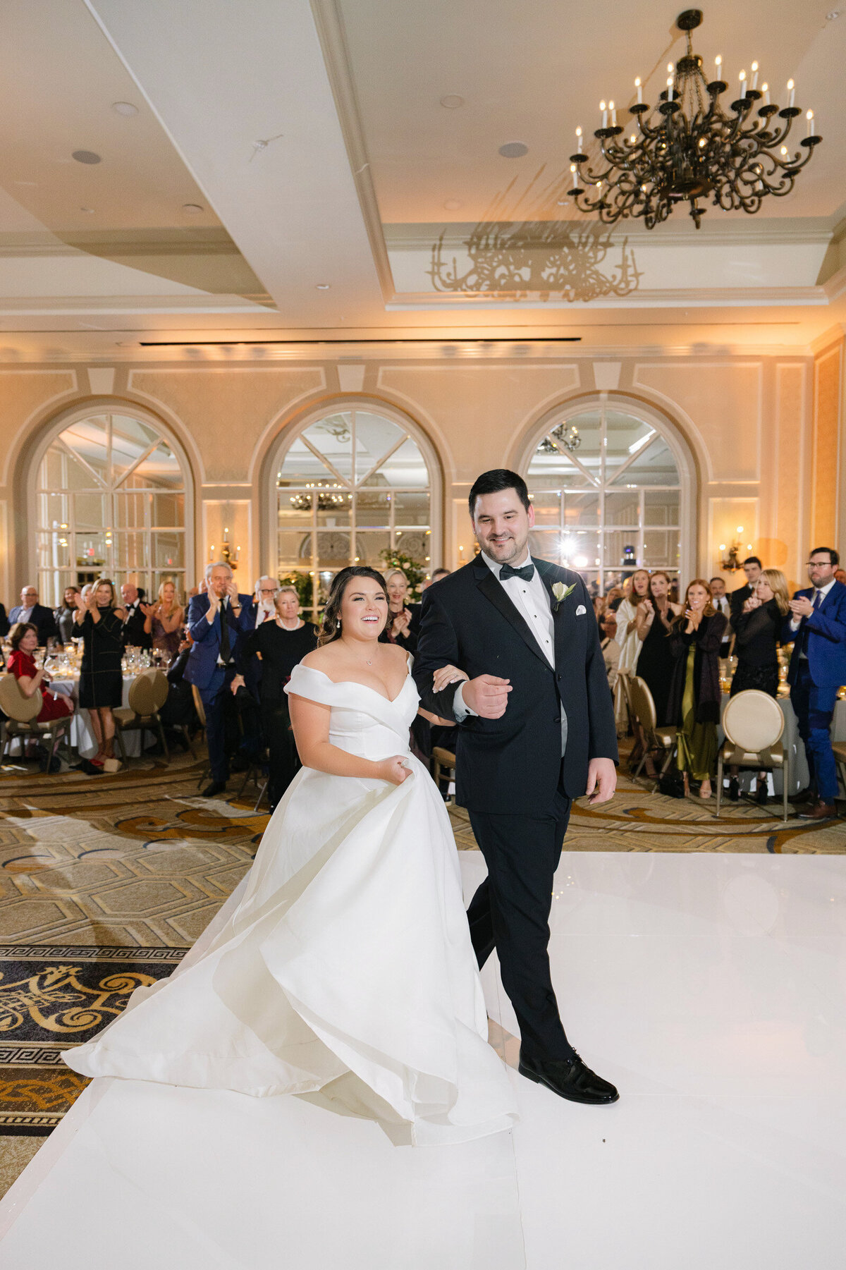 bride and groom entering their wedding reception at The Adolphus in Dallas, captured in a fun and candid moment celebrating with guests.