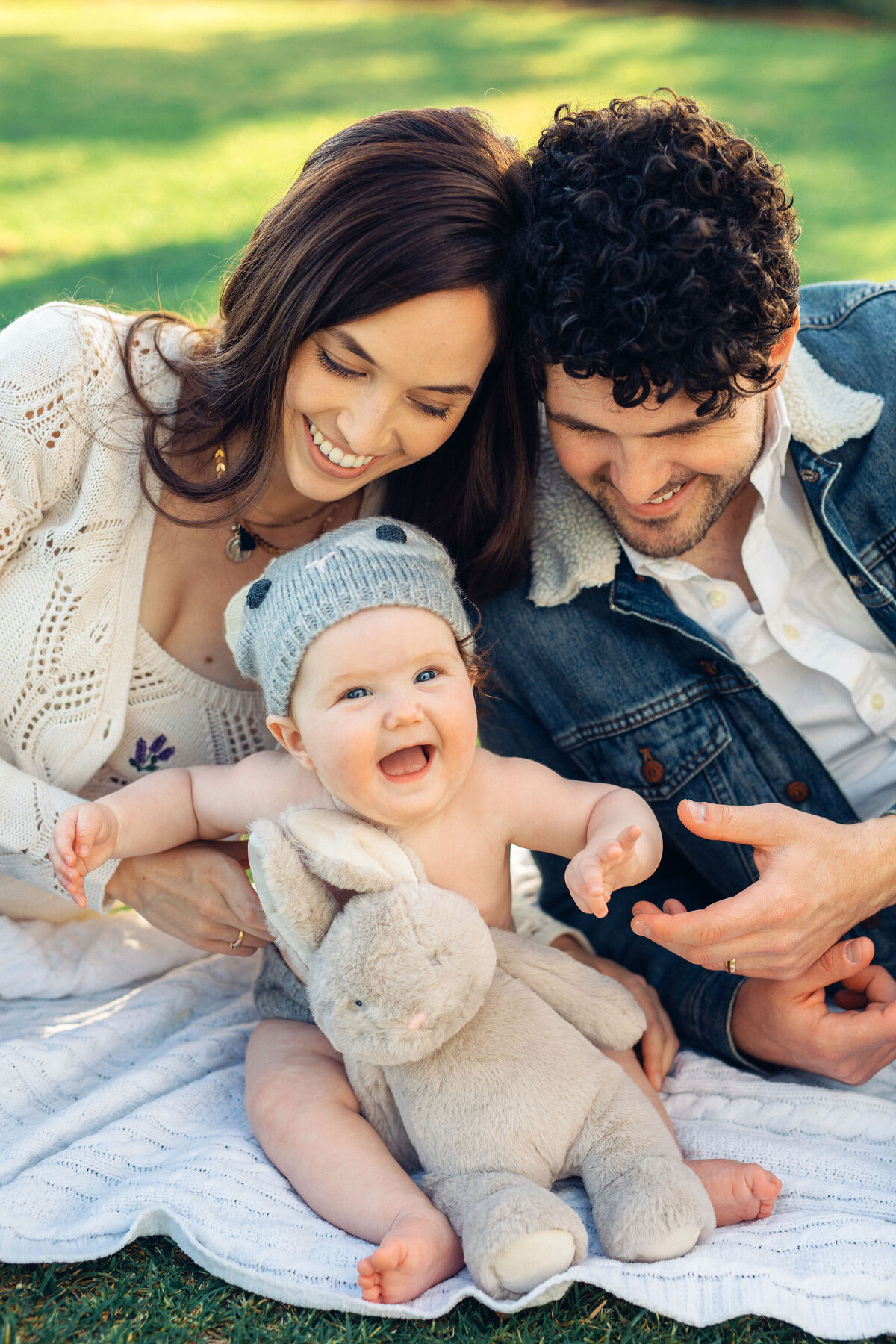 Family Portrait Photo Of Baby Laughing With The Parents  Whiles Sitting On The Ground In los Angeles