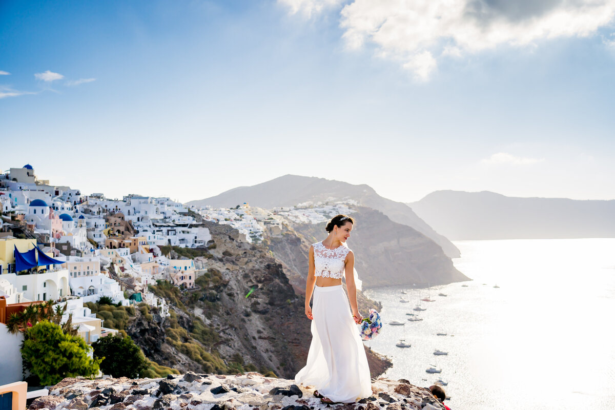 A bride stands on a hillside overlooking the Aegean sea in Santorini Greece