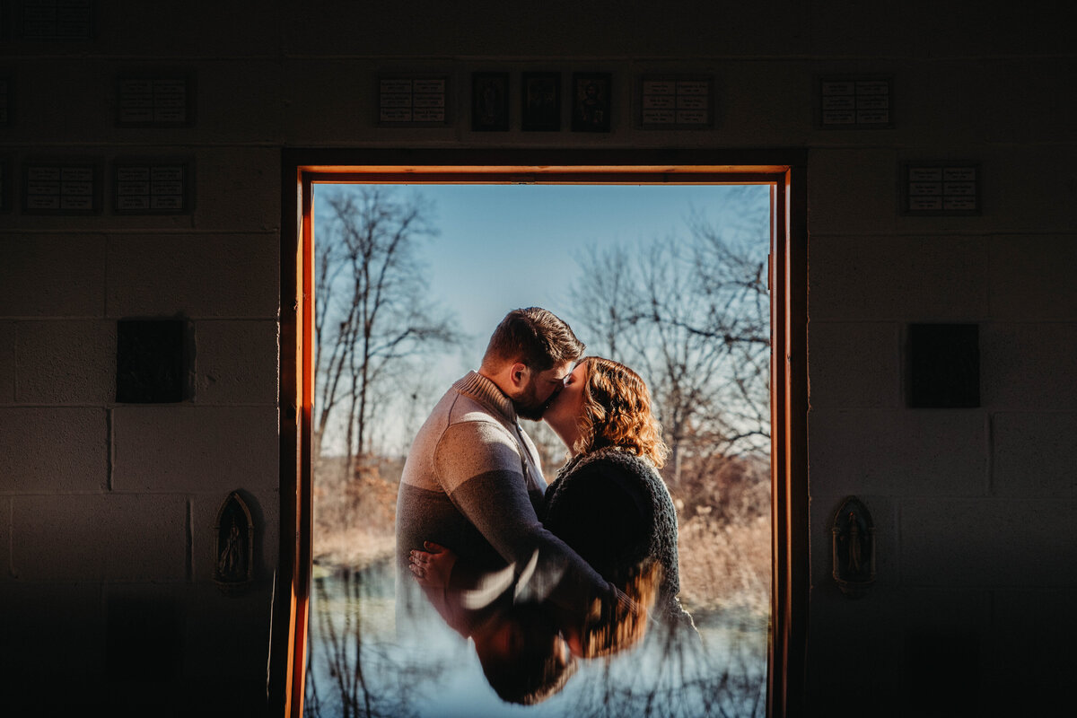 Couple kisses in reflective doorway.